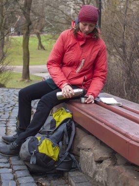 Genç bir kız parkta oturan bir sırt çantası ile.