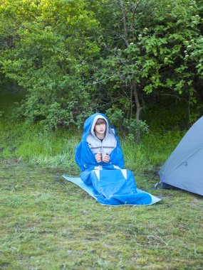 Çadırın yakınında bir uyku tulumu içinde bir adam oturuyor.