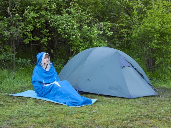 Çadırın yakınında bir uyku tulumu içinde bir adam oturuyor.