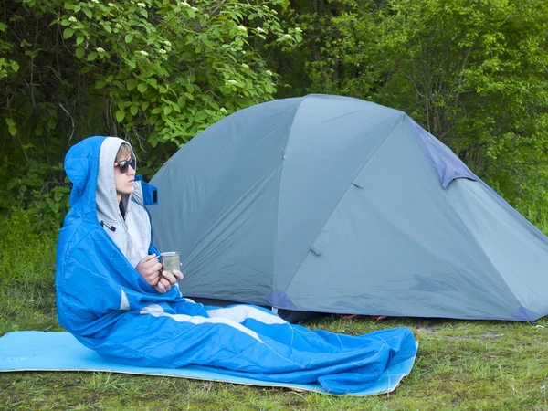 Un homme est assis dans un sac de couchage près de la tente . — Photo