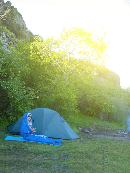 Een man zit in een slaapzak in de buurt van de tent. — Stockfoto