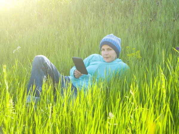 Une jeune fille regarde la tablette couchée sur l'herbe dans le champ — Photo