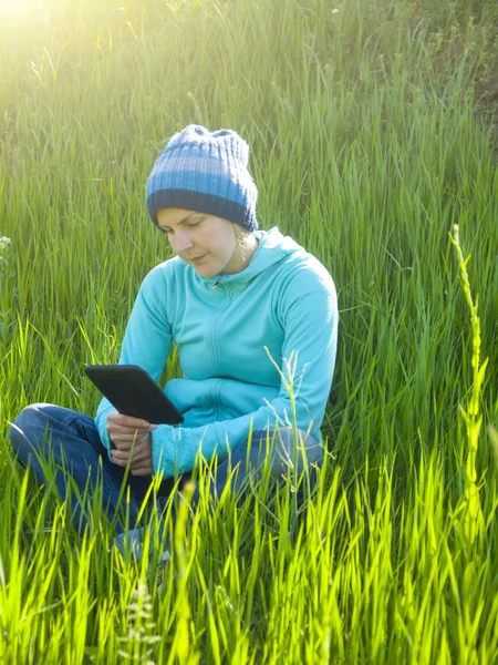 A young girl looks out the tablet lying on the grass in the fiel — Stock Photo, Image