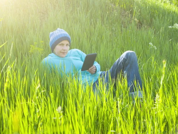 A young girl looks out the tablet lying on the grass in the fiel — Stock Photo, Image