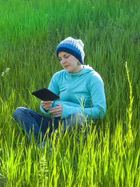 A young girl looks out the tablet lying on the grass in the fiel — Stock Photo, Image