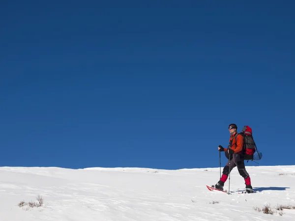 バックパックが付いている山でスノーシューで男は歩く. — ストック写真