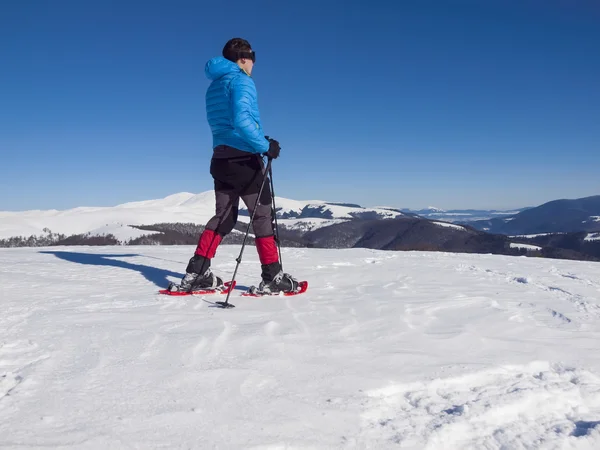 Un hombre en raquetas de nieve es la nieve . — Foto de Stock