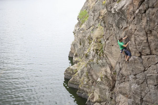 Een man klimt op de rots in de buurt van het water. — Stockfoto