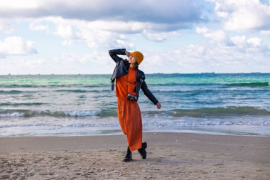 Sırt çantası ve kamerası olan bir kız. Sırt çantalı ve kameralı şık bir kadın soğuk ve güneşli bir günde plaja gitmekten hoşlanır. Yaşam tarzı, seyahat, turizm, doğa, aktif yaşam.