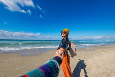 Sahilde erkek arkadaşıyla gezinin tadını çıkaran bir kadın, dikiz manzaralı. Seyahat eden çift. Kız ve erkek el ele tutuşuyor. Sahilde yürü..