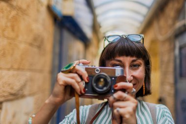Kameralı çekici bir turist. Kameralı güzel bir kadın güzel yerlerin fotoğraflarını çeker. Kız kamerayı yüzüne doğru kaldırır ve fotoğraf çeker. Seyahat ve macera.