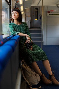Kız kamerayı elinde tutuyor. Elinde kamera olan şık bir kız tren yolculuğunun tadını çıkarıyor. Tren yolculuğu. İyi yolculuklar.