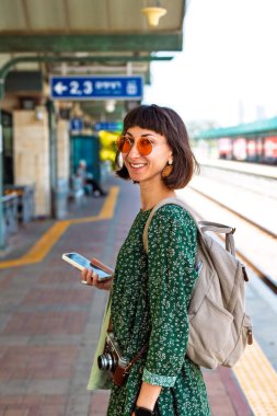 Platformda durmuş tren bekleyen, sırt çantalı şık genç bir kız. Seyahat ve macera.