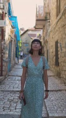 Dikey çekim. Çekici bir turist eski kasabanın caddesi boyunca yürür ve manzaraya bakar. Seyahat ve macera.