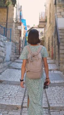 Dikey çekim. Ağır çekim, dikiz aynası, kameralı kadın turist İsrail 'in tarihi şehri Safed' de dar bir sokakta yürüyor.