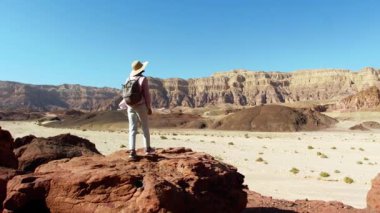Sırt çantalı bir dişi turist çölde yürüyor, kırmızı kayaların ve kanyon geçitlerinin tadını çıkarıyor. Çöl gezisi