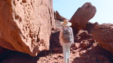Sırt çantalı bir dişi turist çölde yürüyor, kırmızı kayaların ve kanyon geçitlerinin tadını çıkarıyor. Çöl gezisi