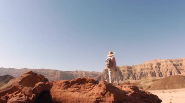 Sırt çantalı genç bir turist çölde yolculuğun tadını çıkarıyor. Sırt çantalı bir kız uçurumun kenarında duruyor ve...