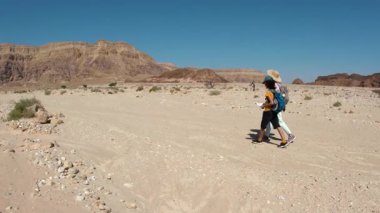 Sırt çantası ve haritası olan bir çocuk çölde annesinin yanında yürüyor. Aile gezisi. Timna Ulusal Parkı. Çocuk.