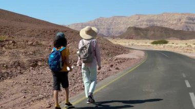 Sırt çantası ve haritası olan bir çocuk çölde annesinin yanında yürüyor. Aile gezisi. Timna Ulusal Parkı. Çocuk.