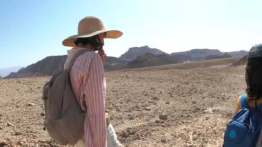 Yürüyüşe çıkmış bir anne ve çocuk. Elinde harita ve sırt çantası olan bir çocuk annesinin yanında yürüyor. Aile gezisi. Timna Ulusal Parkı. Şey...