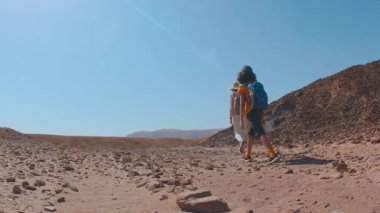 İki aktif gezgin mavi gökyüzüne karşı çölde geziniyor. Anne ve çocuk yürüyüşe çıktı. Yaz kampı. Timna Ulusal Parkı