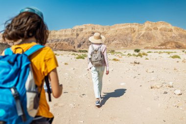 Yürüyüşe çıkmış bir anne ve çocuk. Elinde harita ve sırt çantası olan bir çocuk annesinin yanında yürüyor. Aile gezisi. Timna Ulusal Parkı. Çocuk aktif olarak zaman geçiriyor. Gezinti ve yürüyüş.