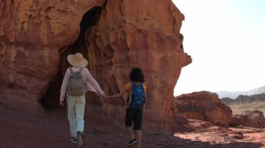 Yürüyüşe çıkmış bir anne ve çocuk. Elinde harita ve sırt çantası olan bir çocuk annesinin yanında yürüyor. Aile gezisi. Timna Ulusal Parkı. Şey...