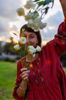 Romantik bir ruh hali. Güzel elbiseli güzel bir kadının portresi ve gün batımında elinde bir buket çiçekle. Kız gülümser ve kameraya bakar..