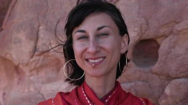 Şehvetli, koyu renk saçlı bir kız rüzgarlı bir çölün arka planında poz veriyor. Piercingli muhteşem bir kadın anın tadını çıkarıyor.