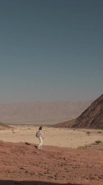 Dikey çekim. Sırt çantalı genç bir turist çölde yolculuğun tadını çıkarıyor. Sırt çantalı bir kız uçlarda duruyor.