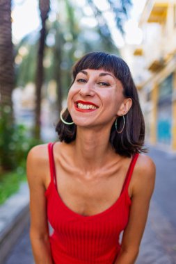 Kırmızı gece elbisesi ve kırmızı ruj sürmüş muhteşem genç bir kadının yakın plan portresi. Kız gülümsüyor ve kameraya bakıyor, tatlı kız, mutlu model.