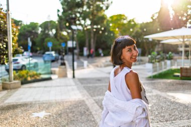Kız güneşli şehir caddesinde yürüyor. Genç kız arkadaşlarıyla buluşacak. şehir tarzı, gülümseme, yaz trendi.