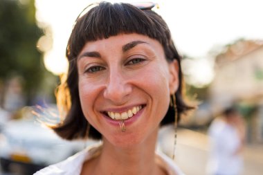 Doğal ışık altındaki genç bir kızın portresi. Kız gülümsüyor ve kameraya bakıyor. Şehir tarzı, yaz trendi.