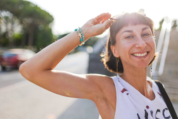 Портрет молодой девушки в естественном свете. Девушка улыбается и смотрит в камеру. Городской стиль, летний тренд.