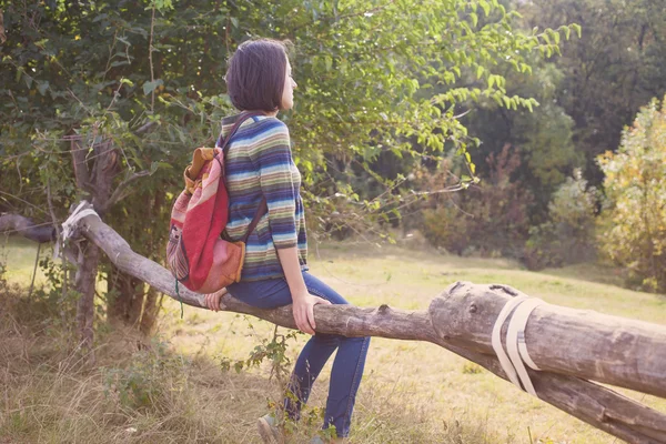 Chica con mochila sentada en la valla y mirando a la naturaleza . — Foto de Stock