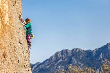 Güçlü bir kız dağlara ve gökyüzüne karşı bir kayaya tırmanır. Aşırı hobi, zor bir tırmanış rotasını aşmak, kadın kaya tırmanışı. Kaya tırmanışı sırasında gayret, Duygusal kız.