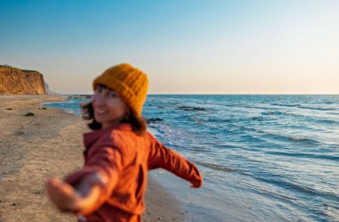 Gülümseyen neşeli kız sahilde eğleniyor anın tadını çıkarıyor. Plajda yürüyen tişörtlü bir kadın. Tatilde bir turist. Seyahat ve macera.