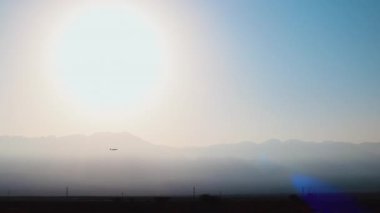 Uçak şafak sökerken gökyüzünde dağların arka planına doğru uçuyor. Uçak iner..