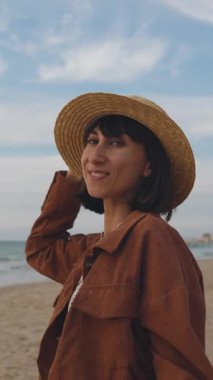 Dikey çekim. Yağmurdan sonra plajda yürürken şapkalı genç bir kadının görüntüsü. Kız eğleniyor