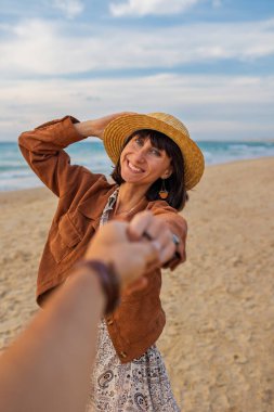 Neşeli bir kız plaj boyunca koşar ve erkek arkadaşının elini tutar. Beni takip edin. Aşık bir kız, erkek arkadaşını deniz kıyısına götürüyor. Sevgililer Günü. Romantik ruh hali.