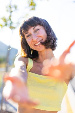 Havalı yaz kıyafetleri içinde, yüzü piercingli, gülümseyen genç bir esmer. Güneşli bir günde dışarıda poz veren baştan çıkarıcı, kaygısız kadın. Açık havada pozitif model. Yaz havası.