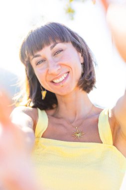 Havalı yaz kıyafetleri içinde, yüzü piercingli, gülümseyen genç bir esmer. Güneşli bir günde dışarıda poz veren baştan çıkarıcı, kaygısız kadın. Açık havada pozitif model. Yaz havası.