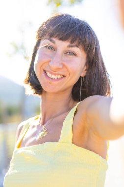 Havalı yaz kıyafetleri içinde, yüzü piercingli, gülümseyen genç bir esmer. Güneşli bir günde dışarıda poz veren baştan çıkarıcı, kaygısız kadın. Açık havada pozitif model. Yaz havası.