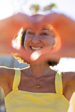 Gün batımında sevişen gülümseyen kız. Romantik ruh hali. Genç, gülümseyen, çekici bir kadının portresi. Elleriyle kalbi gösteriyor. Yüzünde parlayan bir gülümseme..