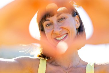 Gün batımında sevişen gülümseyen kız. Romantik ruh hali. Genç, gülümseyen, çekici bir kadının portresi. Elleriyle kalbi gösteriyor. Yüzünde parlayan bir gülümseme..