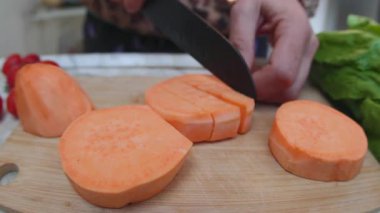 Bir adam tahta bir kesme tahtasında tatlı patatesleri dilimliyor. Sağlıklı beslenme. Yakın plan..