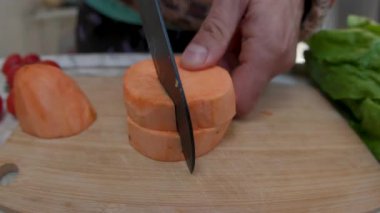 Bir adam soyulmuş patatesi tahta bir kesme tahtasının üzerinde dilimlere ayırıyor. Sağlıklı beslenme. Yakın plan..