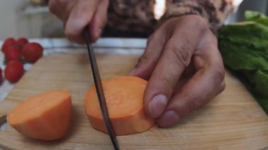 Vejetaryen yemeği hazırlıyorum. Bir adam soyulmuş tatlı patatesi tahta bir kesme tahtasıyla dilimliyor. Sağlıklı beslenme. Yakın plan..