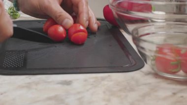 Kirazlı domates kesen bir adam. Kesme tahtasında taze sebzeler. Sağlıklı beslenme.